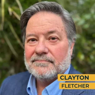 A man with gray hair and a beard, wearing a blue collared shirt and blazer, stands in front of a blurred nature background. The text "Clayton Fletcher" appears in yellow at the bottom right.