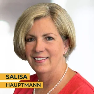 A woman with short blonde hair and wearing a red top and pearl necklace is smiling at the camera. The text "Salisa Hauptmann" appears in the bottom left corner.