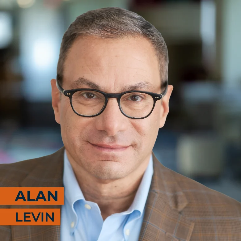 Man with short brown hair and glasses wearing a plaid blazer and blue shirt, standing indoors. Text overlay reads "ALAN LEVIN.