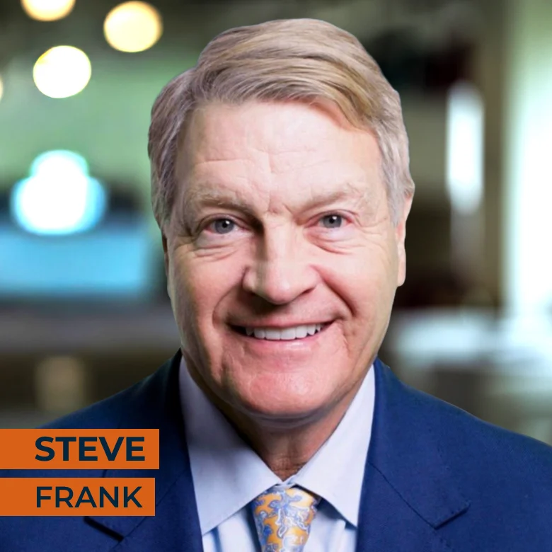 Smiling middle-aged man in a blue suit and tie, with short light hair, standing indoors. Text on image reads "Steve Frank.