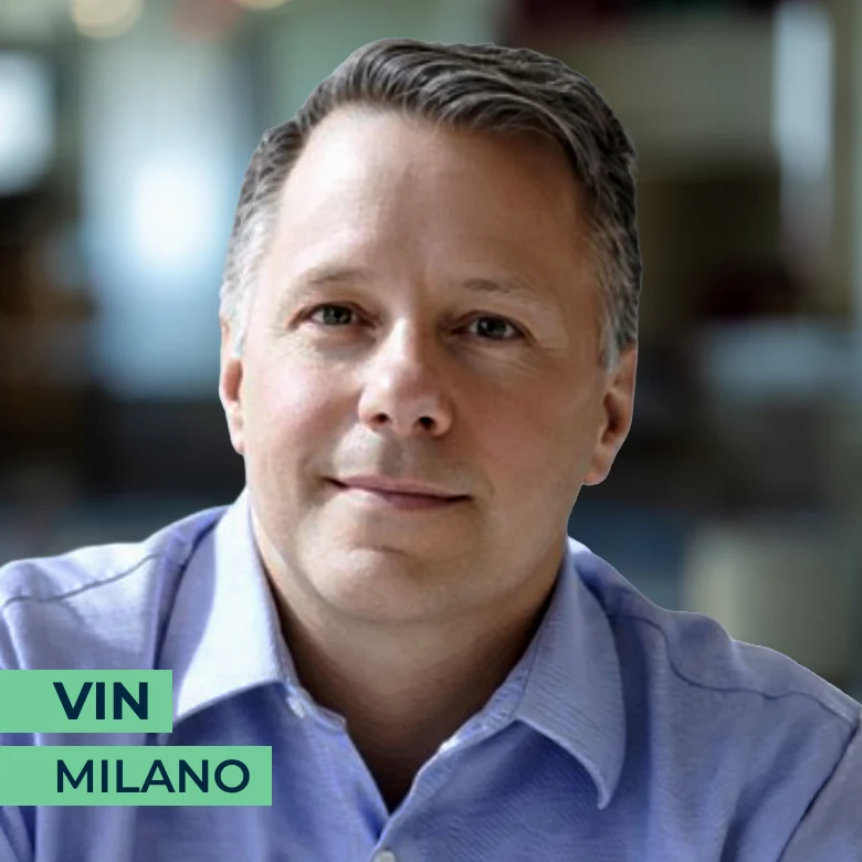 A middle-aged man with short gray hair wearing a light blue collared shirt. The text overlay reads "VIN MILANO." The background is softly blurred.